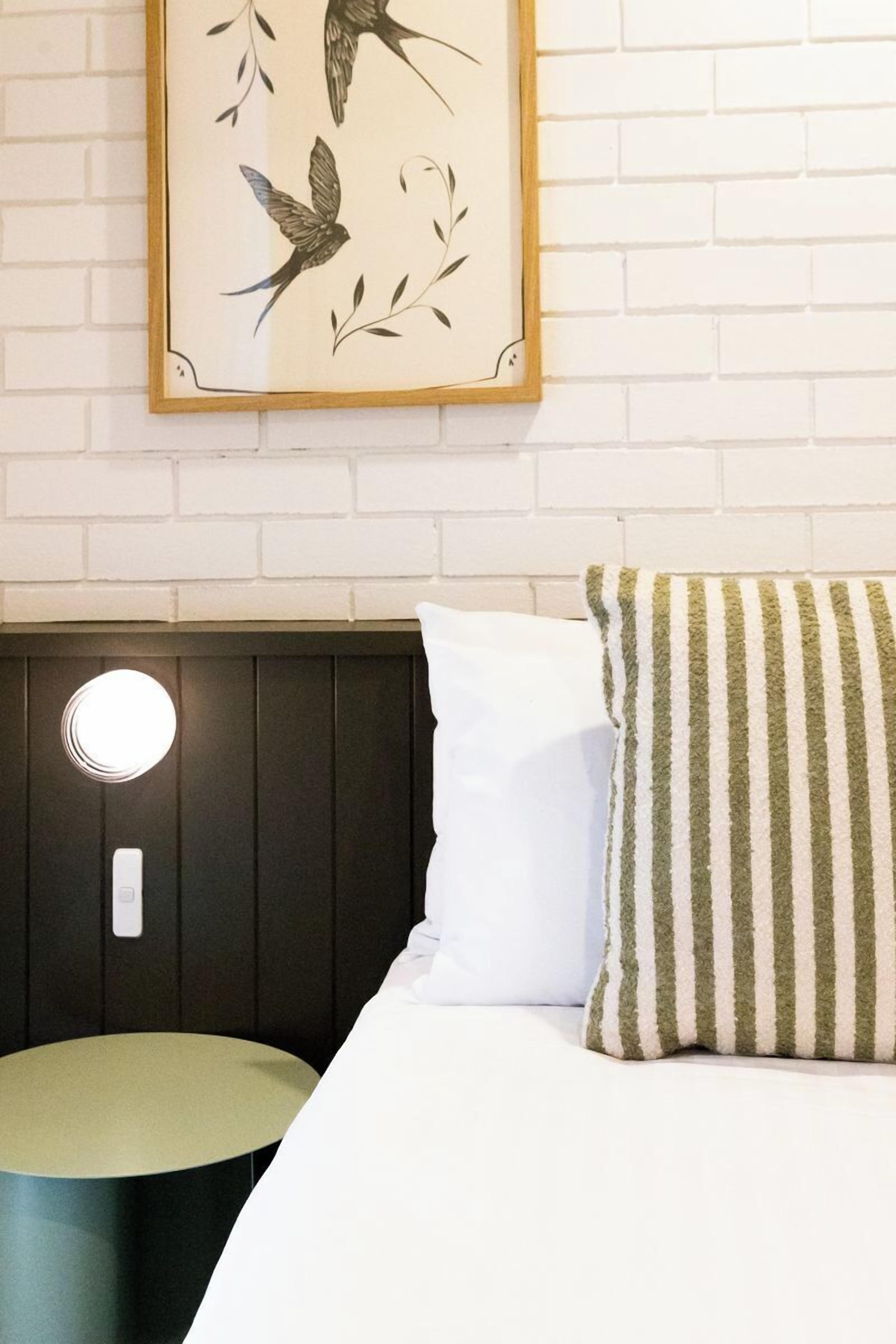 A neatly made bed with a striped pillow, a white pillow, and a framed picture of birds on the wall.