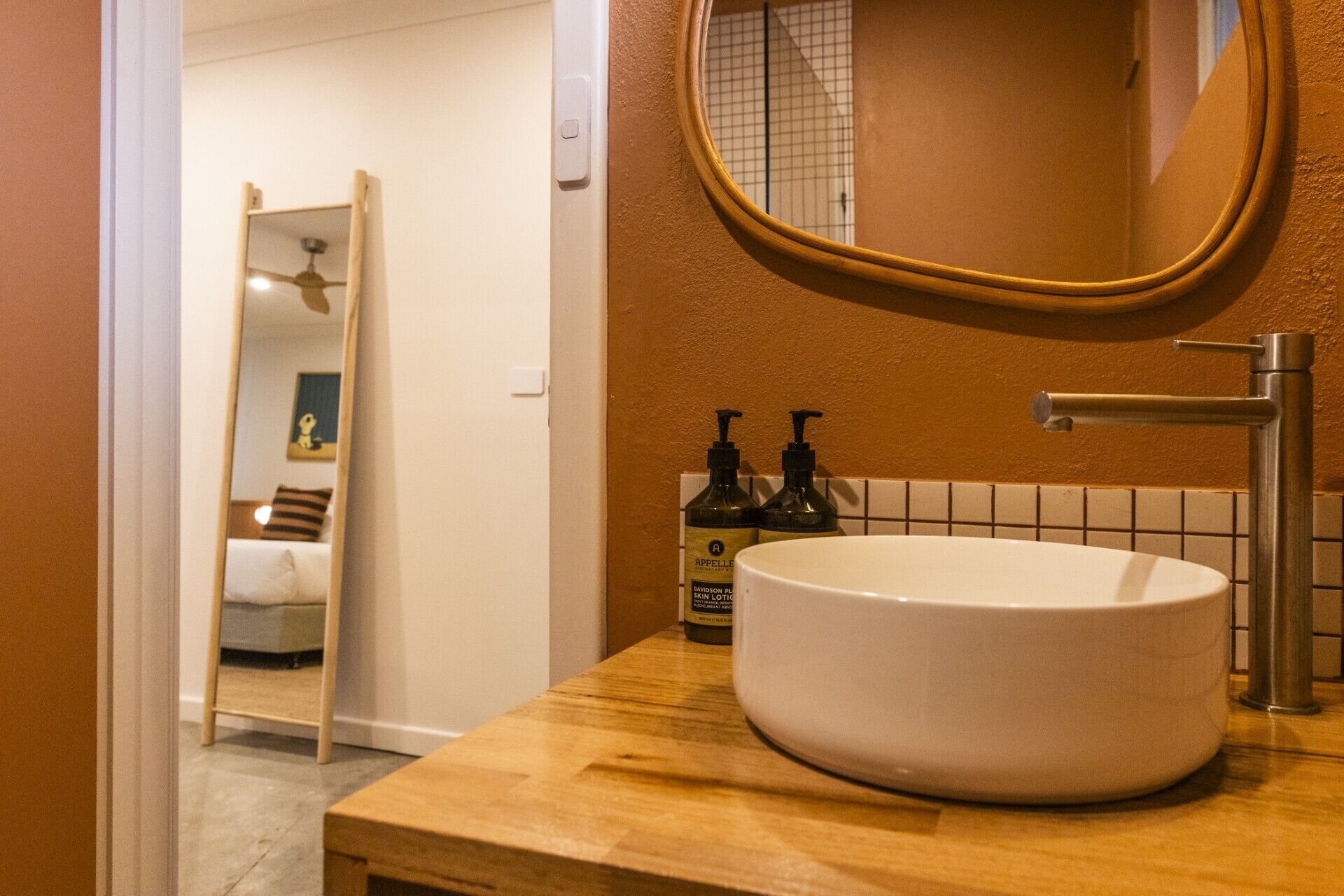 A bathroom with a round mirror, a white sink, and two bottles of hand soap on the countertop.