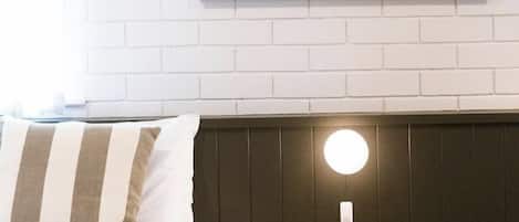 A hotel room with a bed, a round wall-mounted light, a small round table, and a framed artwork on the wall.