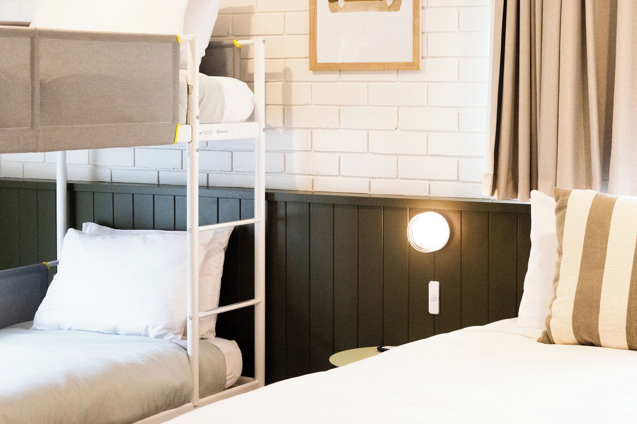 A bunk bed with a headboard, a bedside table, a wall-mounted light, and a framed picture on the wall.