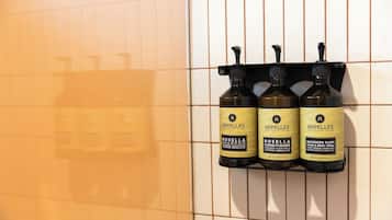 A bathroom with a tiled wall and a shelf holding three bottles of Apelles products.