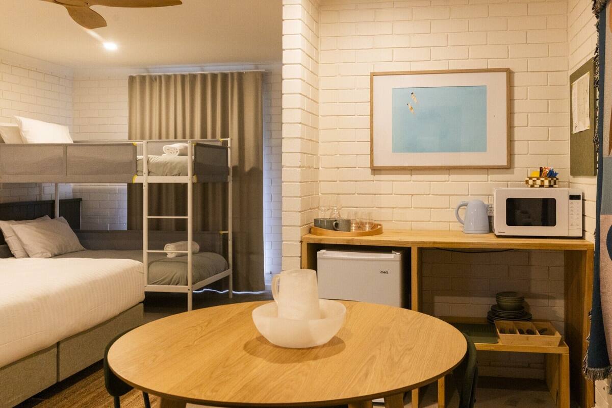 A hotel room with a bunk bed, a round wooden table with a white vase, a microwave, and a small refrigerator.