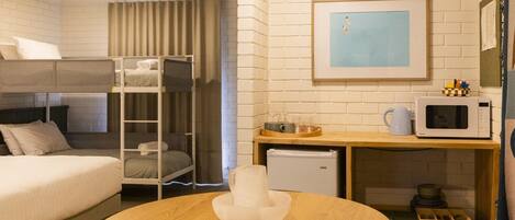 Habitación de hotel con una litera, una mesa redonda de madera con un jarrón blanco, un microondas y un refrigerador pequeño.