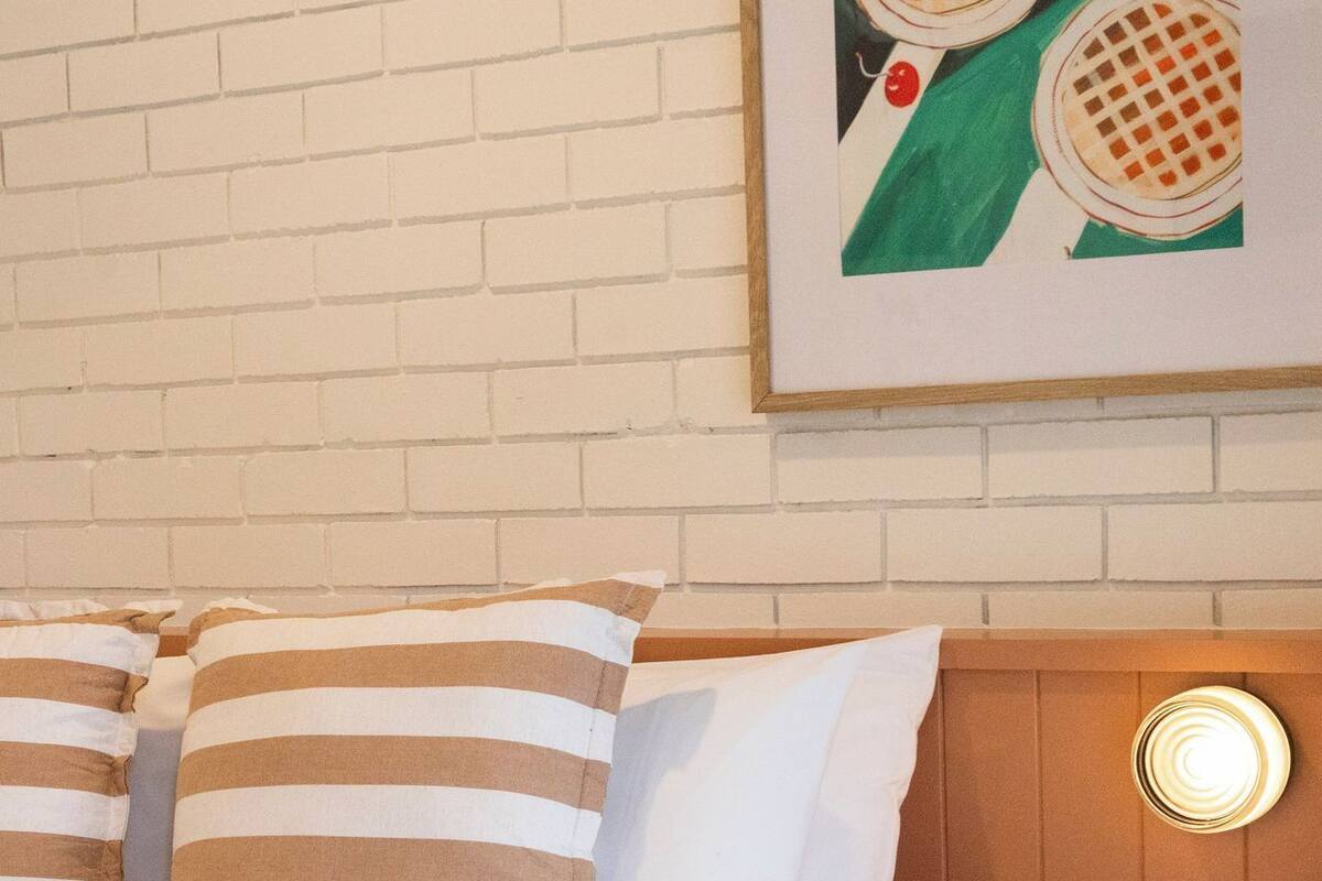 A hotel room with a brick-patterned wall, a bed with striped pillows, and a round wooden table.