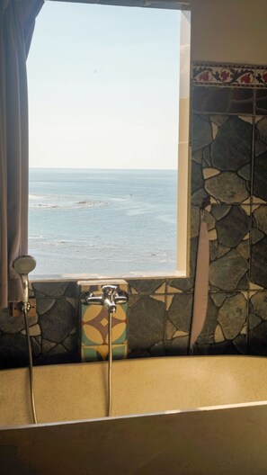 A bathroom with a bathtub, a shower, and a window overlooking the sea. - Kalimaja Amed Villa (Karangasem)