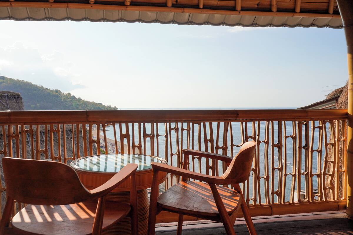 Ein Balkon mit Tisch und Stühlen, der Blick auf eine Küstenlandschaft mit felsigem Gelände bietet.