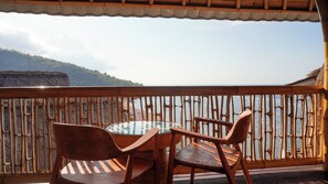 A balcony with a table and chairs, overlooking a coastal view with a rocky landscape. - Kalimaja Amed Villa (Karangasem)