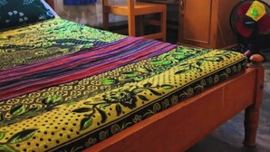Une pièce comprenant un lit, une chaise en bois, un bureau et un ventilateur.