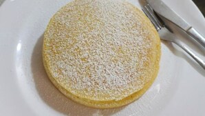 Un gâteau rond et jaune, saupoudré de sucre glace, présenté sur une assiette blanche.