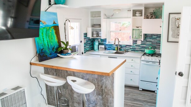 A modern kitchen with a central island, bar stools, a stove, and a sink.