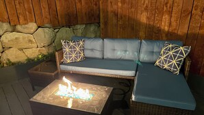 An outdoor seating area with a stone wall backdrop, a fire feature, and a woven bench.
