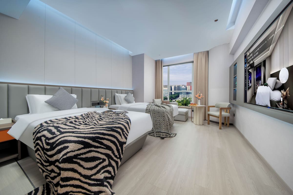 A modern hotel room with a large bed, a seating area, and a city view.