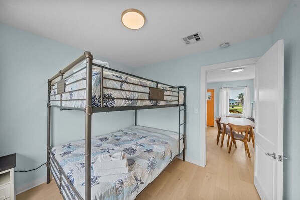 A bunk bed room with a desk and chair, a dining table with chairs, and a door leading to another room.