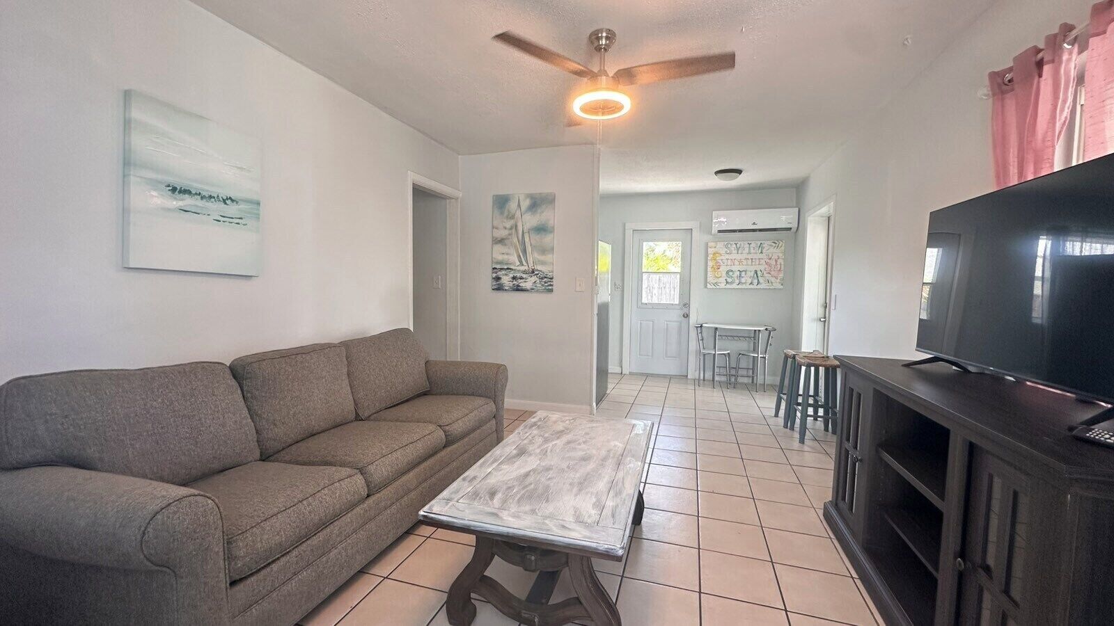 A living room with a sofa, a coffee table, a TV on a stand, and a ceiling fan.