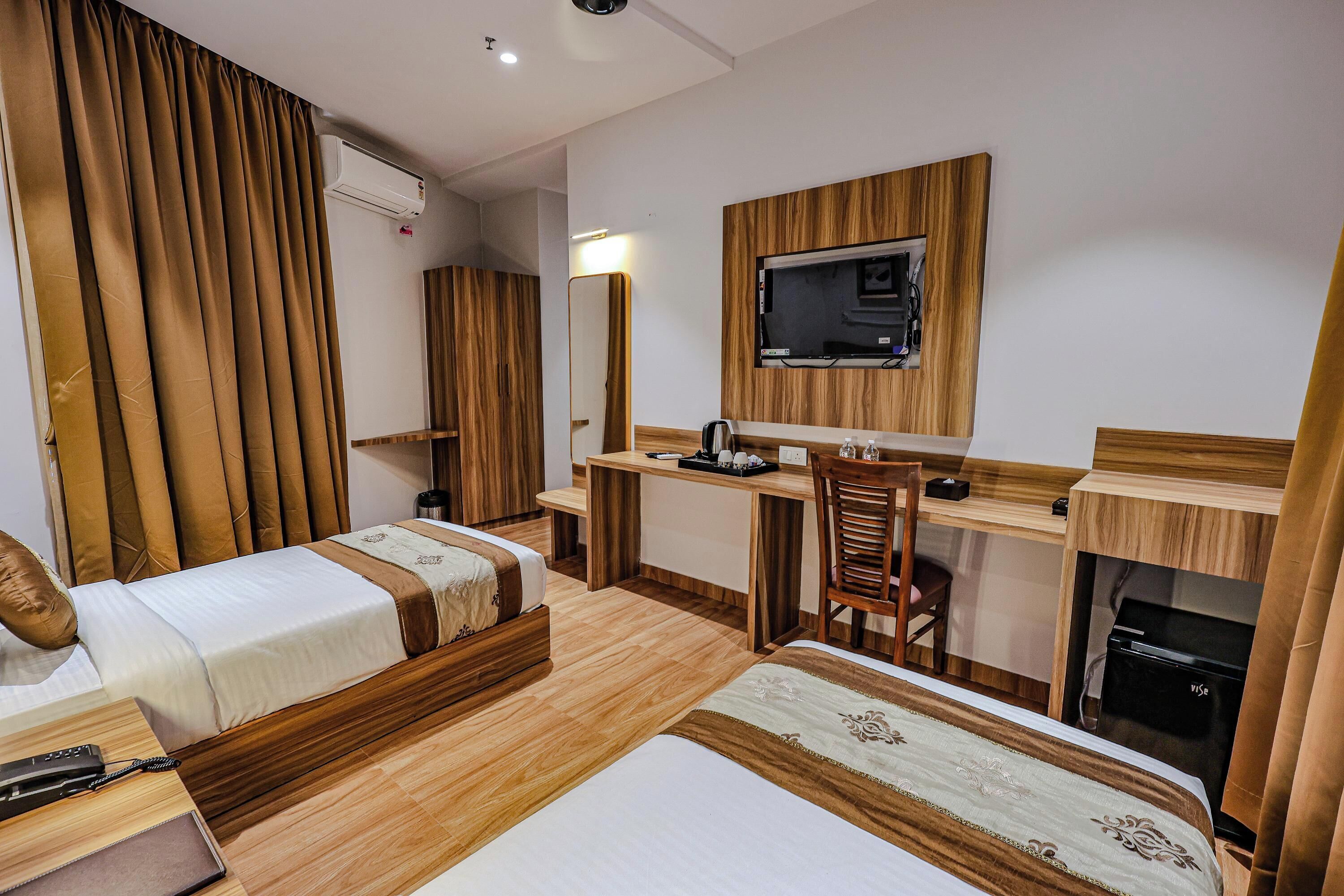 A hotel room with two beds, a desk, a chair, a TV, and a minibar.