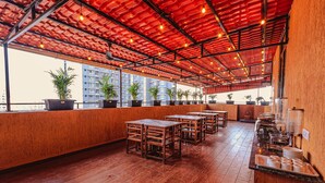 A rooftop restaurant with wooden tables and chairs, potted plants, and a red ceiling. - Hotel Alfa Suites (Mumbai)