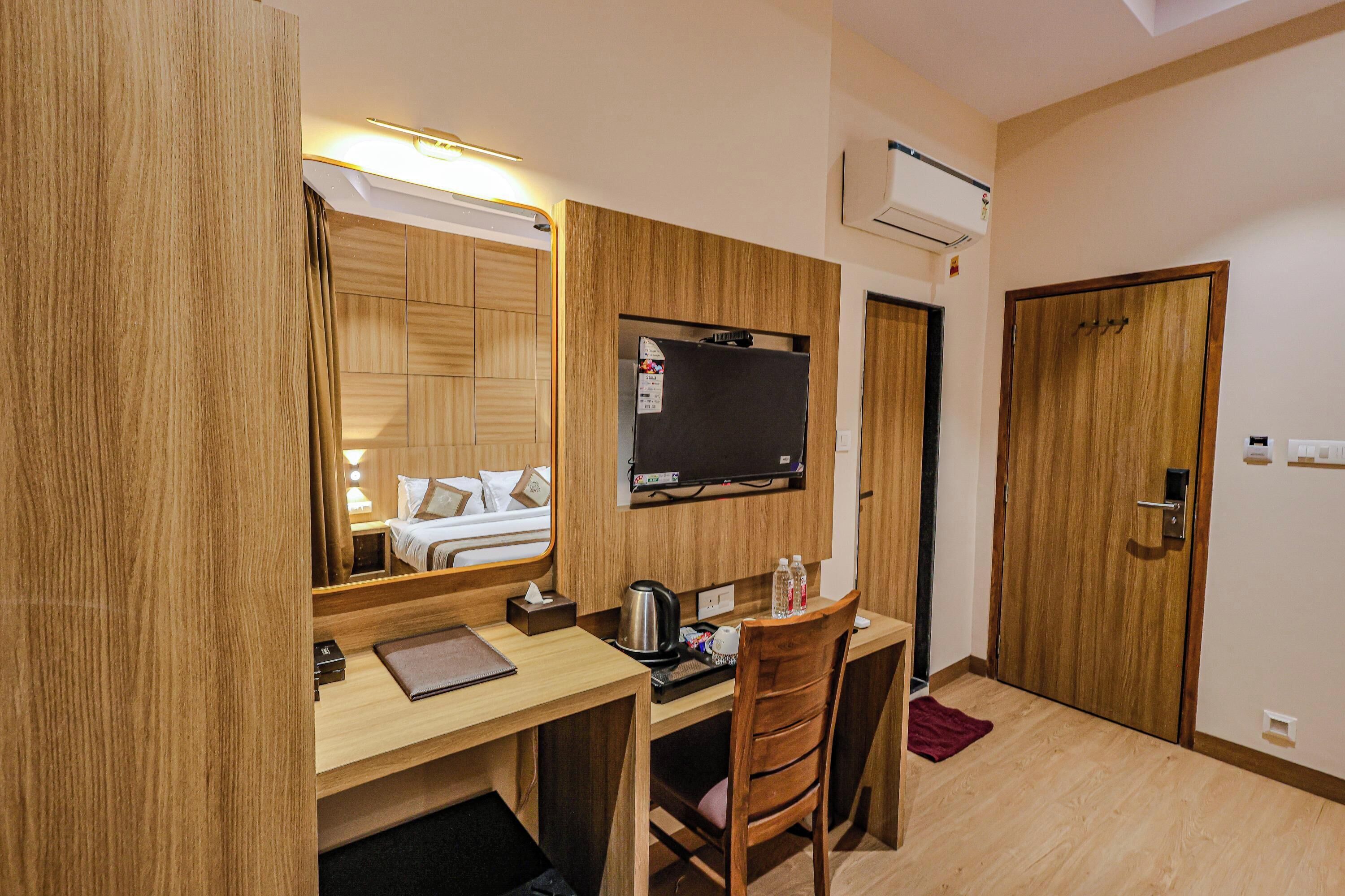 Een hotelkamer met een houten bureau, stoel, bed en een wandgemonteerde televisie.
