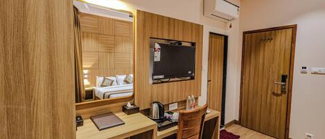 Een hotelkamer met een houten bureau, stoel, bed en een wandgemonteerde televisie.
