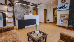 A hotel reception area with a modern design, including a reception desk, a clock, and a television displaying a dog. - Hotel Alfa Suites (Mumbai)