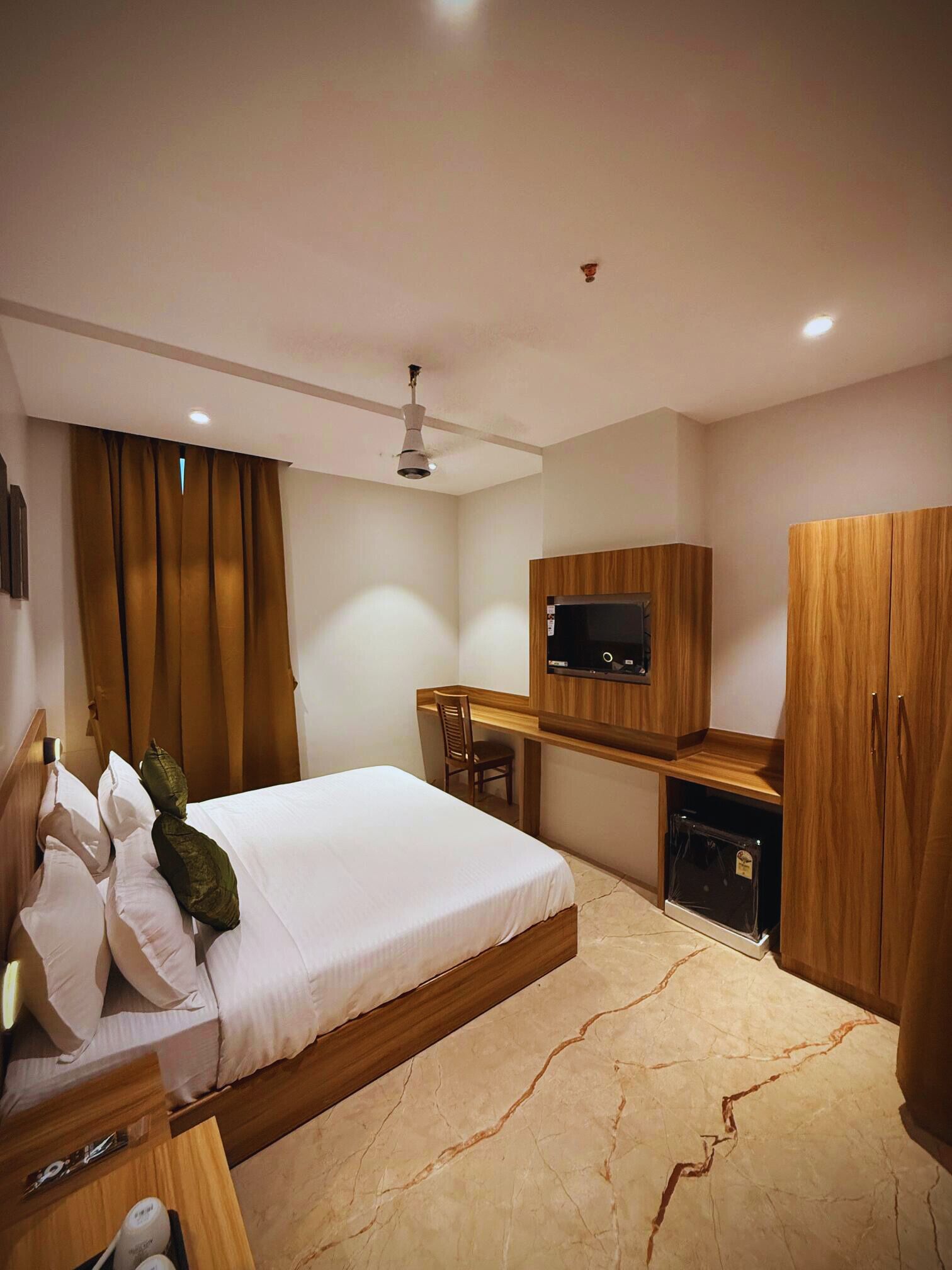 A modern hotel room with a bed, desk, wardrobe, and a flat-screen TV.