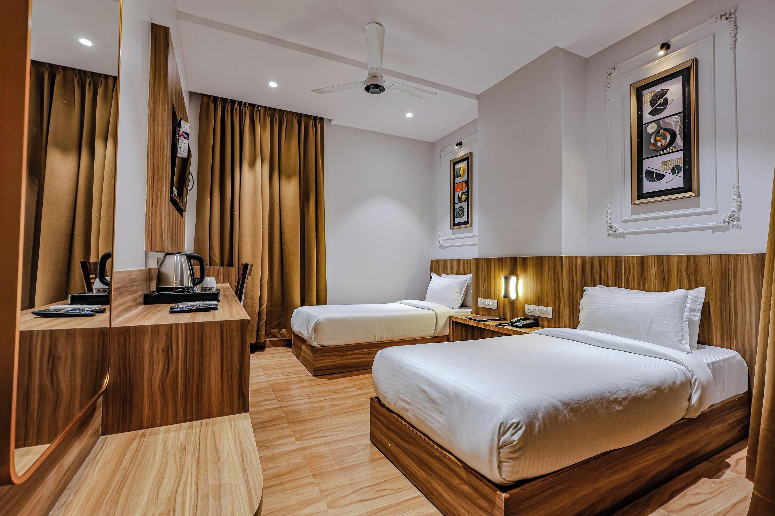 Habitación de hotel con dos camas, un escritorio de madera, ventilador de techo y un cuadro en la pared.