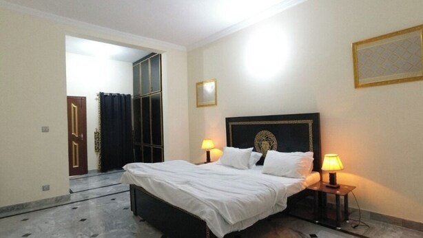 A bedroom with a bed, two bedside lamps, a mirror, and a door leading to another room. - Room-charming B&B in Rawalpindi Familie (Rawalpindi)