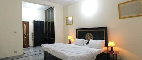 A bedroom with a bed, two bedside lamps, a mirror, and a door leading to another room.