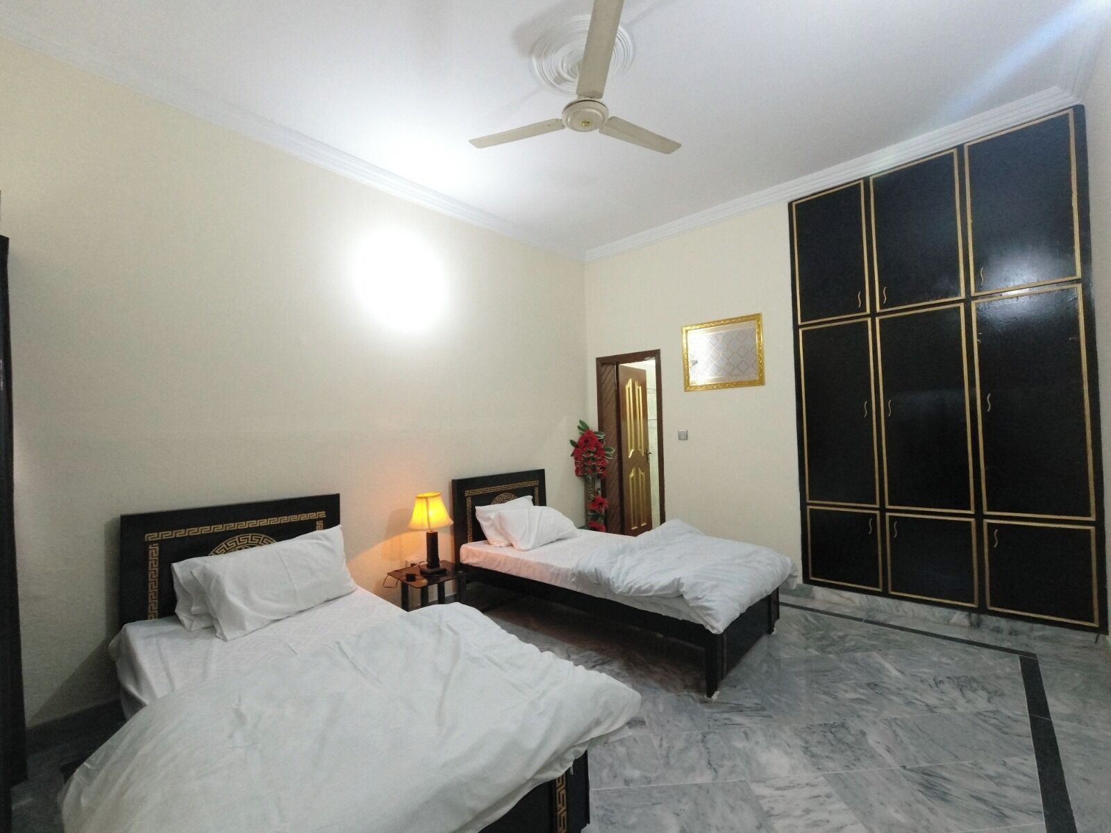 Una habitación de hotel con dos camas, ventilador de techo, mesita de noche con lámpara, espejo y armario.