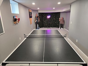 Una mesa de ping pong en una habitación con paredes grises, un ventanal pequeño y un letrero de neón.
