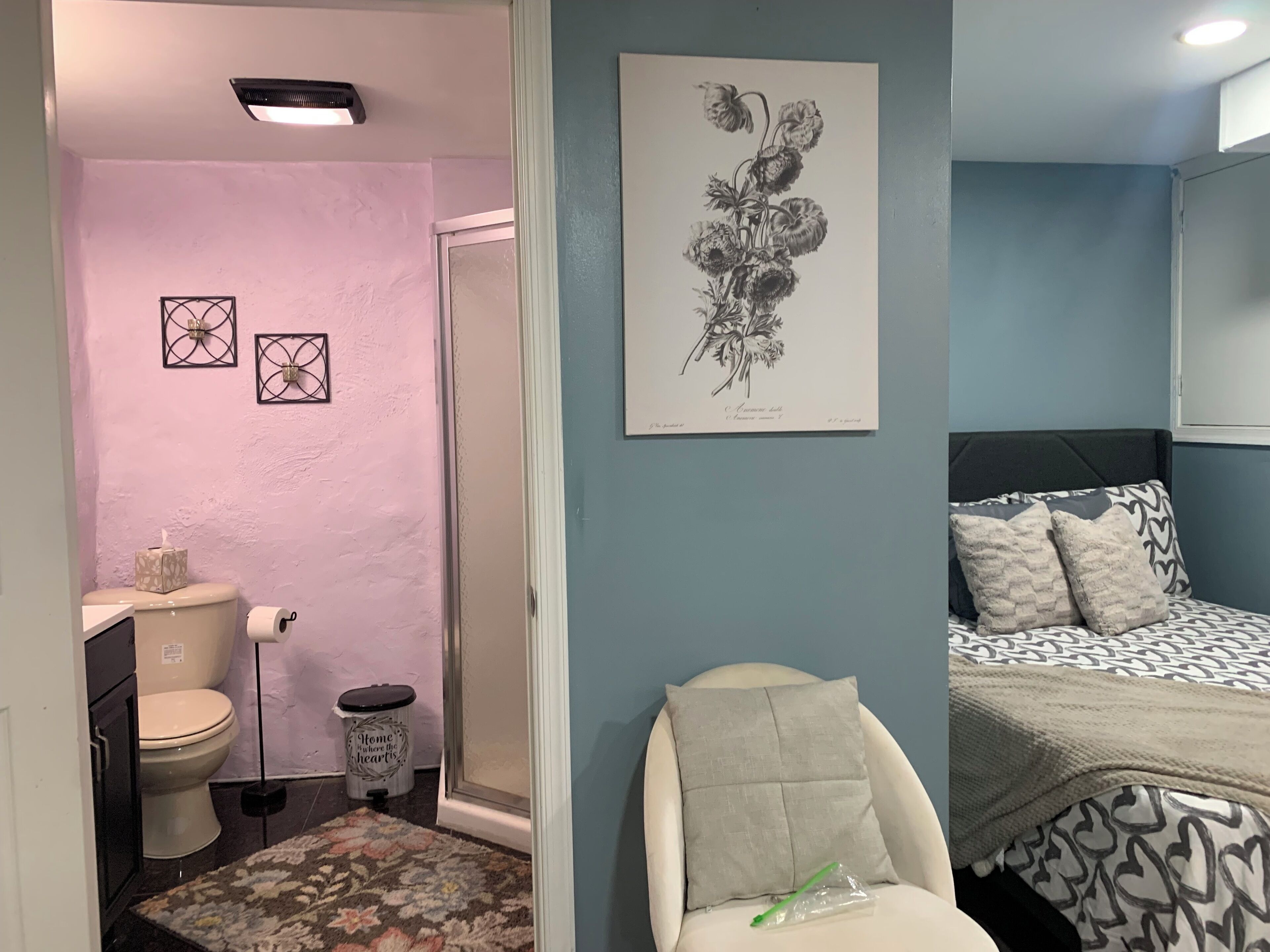 A bathroom with a toilet, sink, and a trash can. There is a rug on the floor and a chair with a pillow.