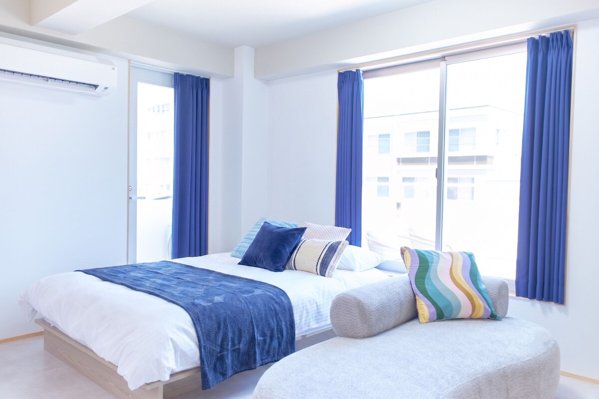 A modern hotel room with a bed, a chair, and large windows with curtains.