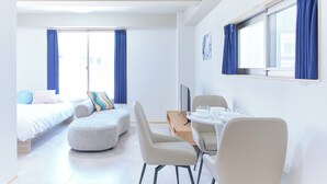 Una habitación de hotel moderna con cama, sofá, una mesa de comedor con sillas, televisor y ventana con cortinas.