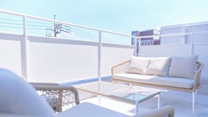 Un balcón con un sofá blanco, sillas de mimbre y una mesa de vidrio.
