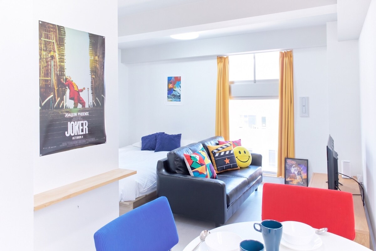 A modern hotel room with a bed, a sofa, a dining table, and a TV.