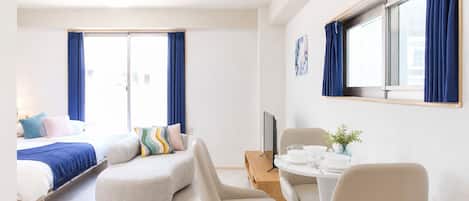 A modern hotel room with a bed, a sofa, a dining table with chairs, and a TV.