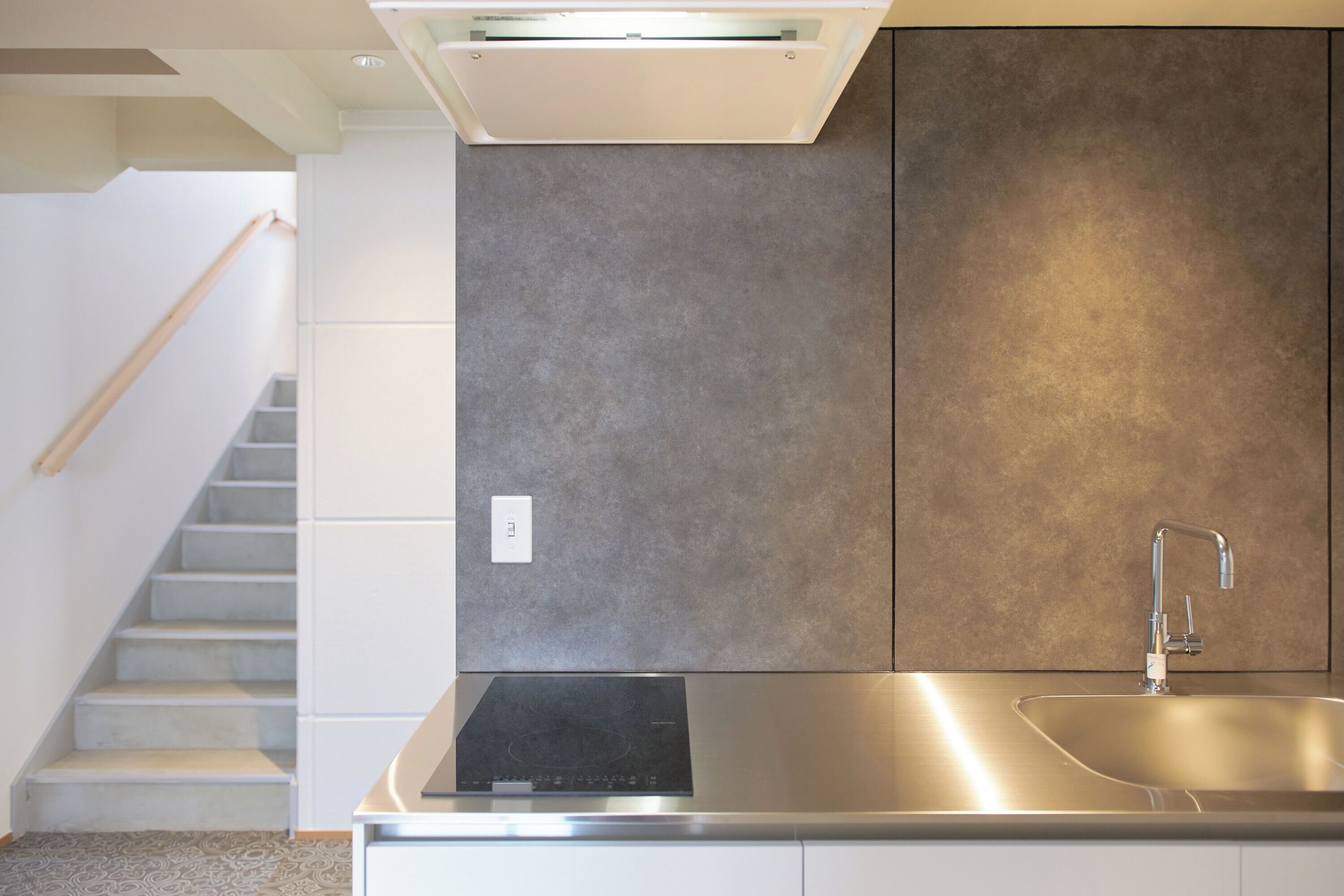 A modern kitchen with a stainless steel sink, a built-in stove, and a staircase leading to another level.