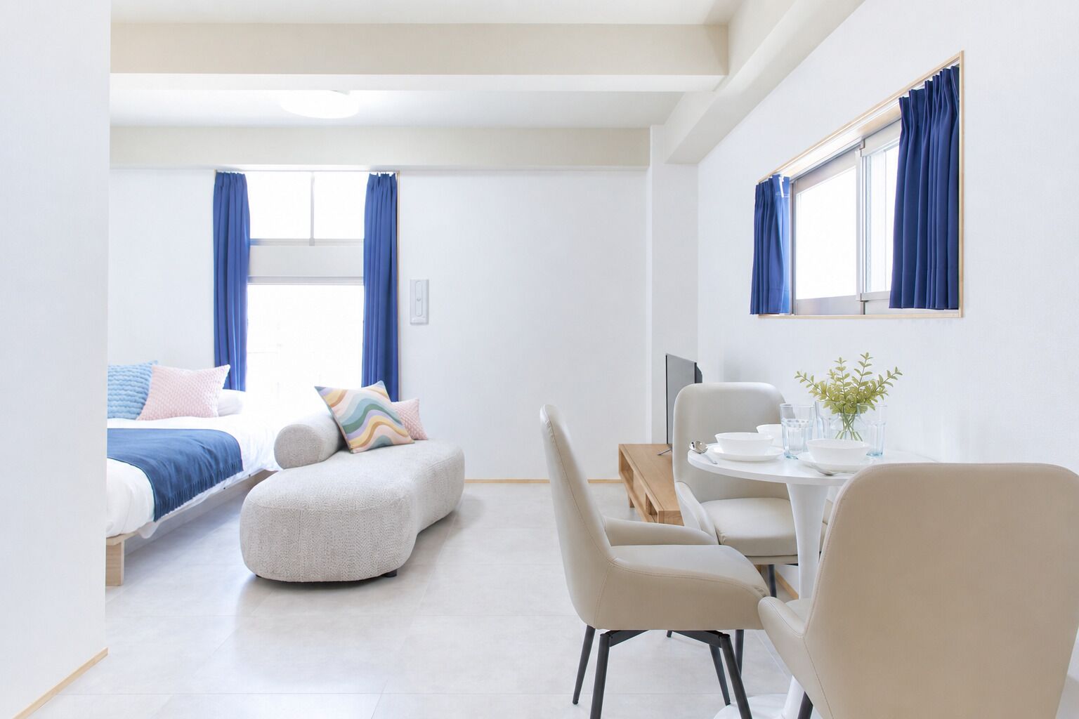 Quarto de hotel moderno com cama, sofá, mesa de jantar com cadeiras e televisão.
