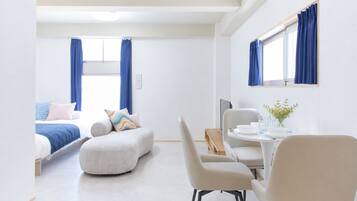 Quarto de hotel moderno com cama, sofá, mesa de jantar com cadeiras e televisão.