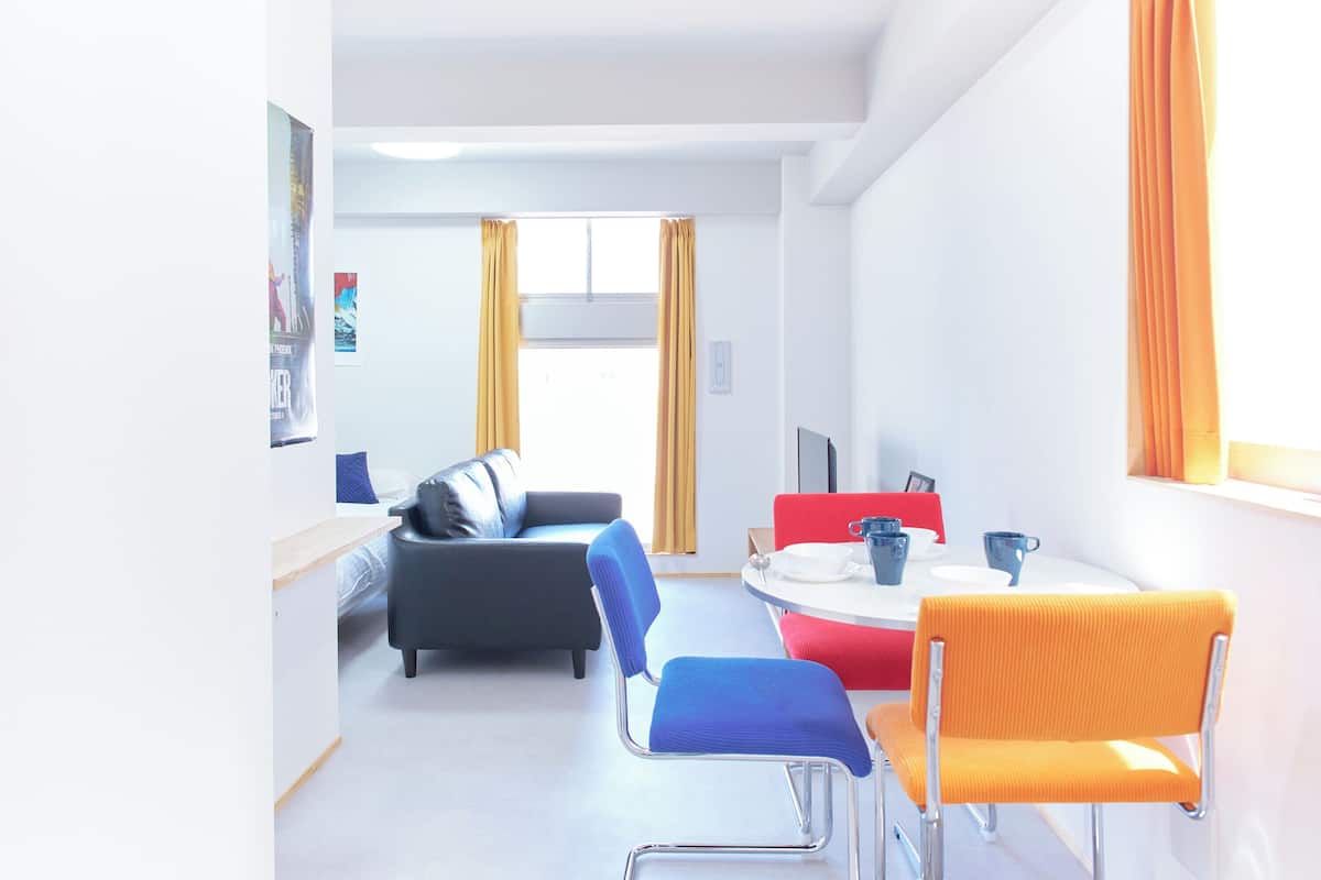 A modern hotel room with a bed, a desk, a chair, a dining table, and a window with curtains.