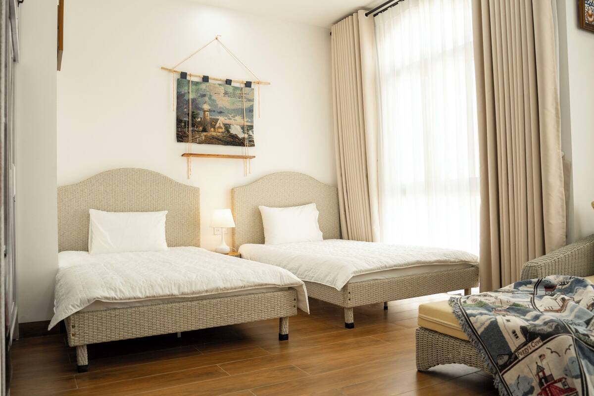 Een hotelkamer met twee enkele bedden, een kleine zithoek, een wandtapijt en een raam met gordijnen.