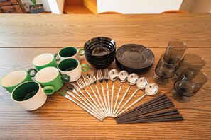Ein Holztisch mit grünen und weißen Tassen, schwarzen Schüsseln, silbernen Löffeln und klaren Gläsern.