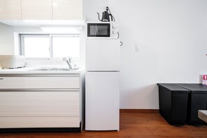 A modern kitchen with white cabinets, a white refrigerator, a microwave, and a black coffee maker on the counter. - Tokyo Home Base Haneda (Tokyo)