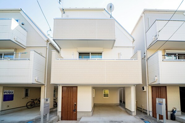 A two-story residential building with a central entrance, a small balcony on the upper floor, and a bicycle parked outside. - Tokyo Home Base Haneda (Tokyo)
