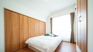 Une chambre avec une armoire en bois, un lit avec une literie blanche et une fenêtre avec des rideaux.