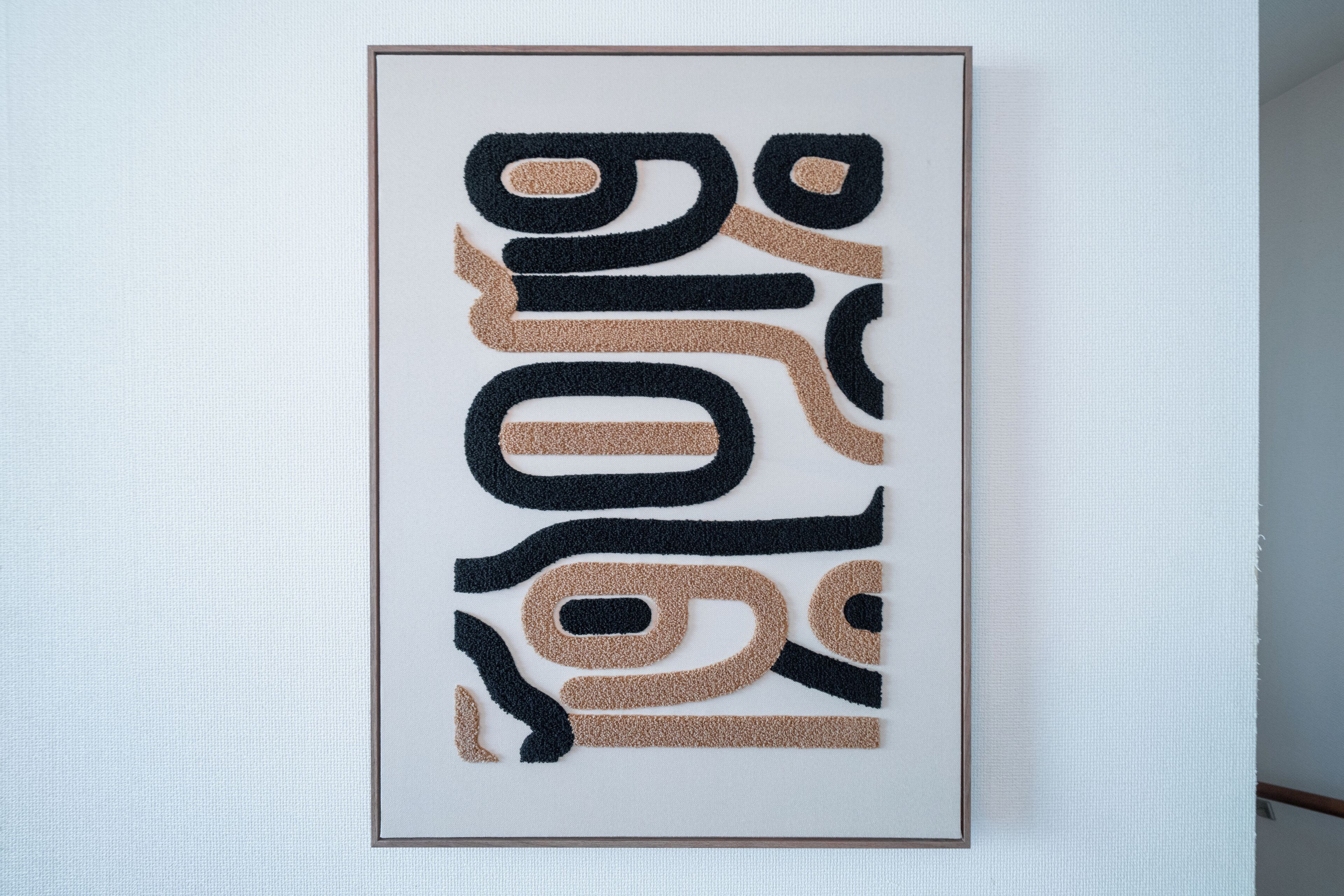 A framed abstract art piece with black and beige colors.
