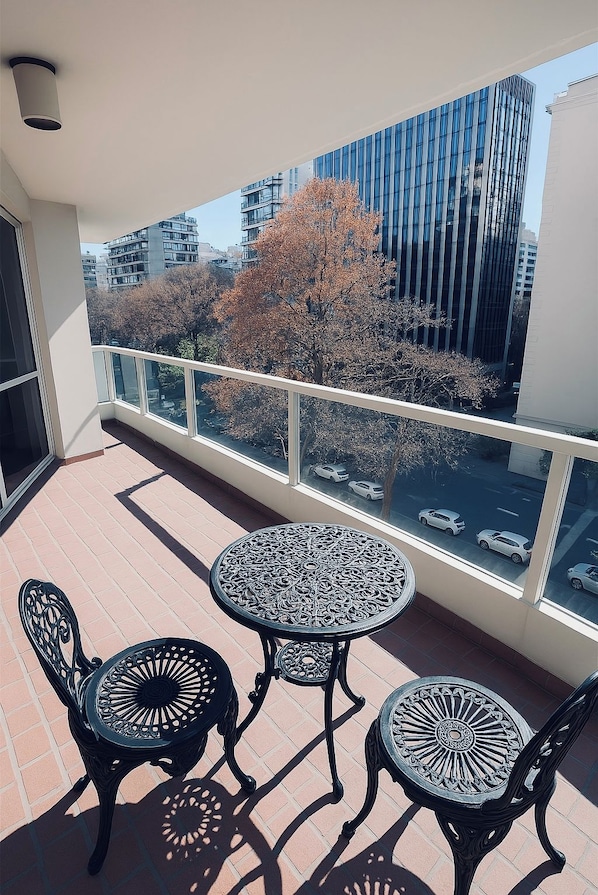 A balcony with a table and chairs, a railing, and a view of buildings and trees.