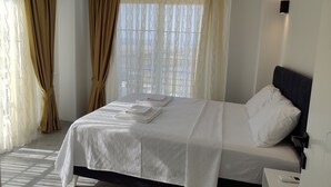 A neatly made bed with white linens, a bedside table with a remote control, and sheer curtains with a wavy pattern. - Villa Beyaz İnci Dalaman-Villa White Pearl Dalaman (Dalaman)