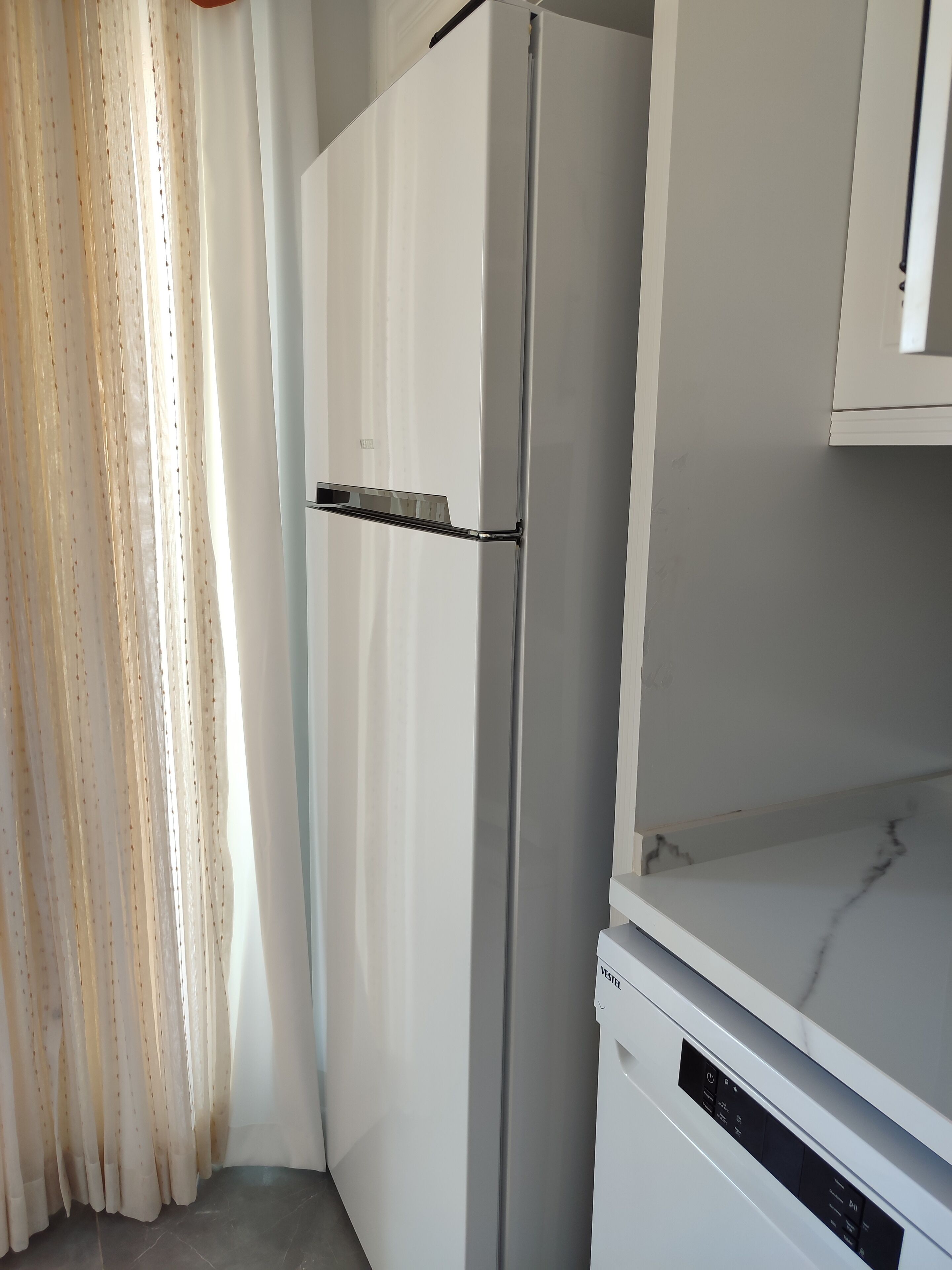 A white refrigerator with a freezer compartment, a white countertop, and a white cabinet above it.