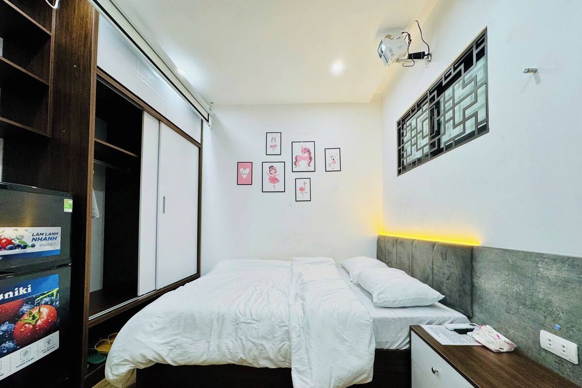 A bedroom with a bed, bedside table, wardrobe, and wall-mounted projector.