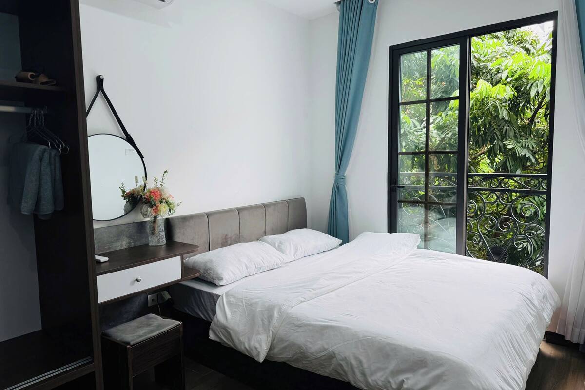A bedroom with a bed, a bedside table, a mirror, a wardrobe, and a window with curtains.